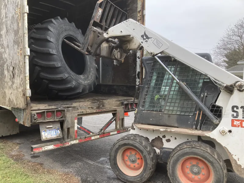 Tractor Tire being loaded by bobcat into trailer