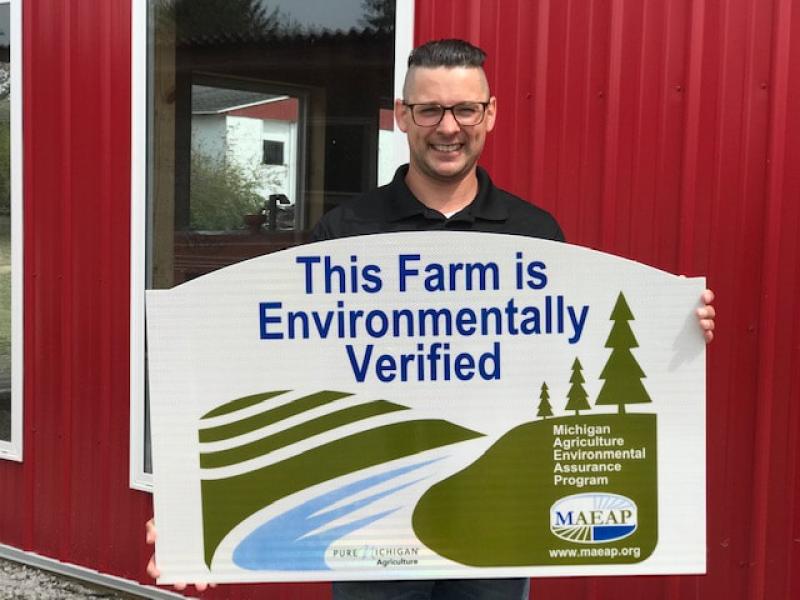 Farmer producer hold a "This Farm is Environmentally Verified" MAEAP sign