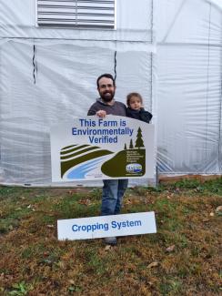 MAEAP - Father and child with "This Farm is Environmentally Verified - Cropping System" sign in front of greenhouse