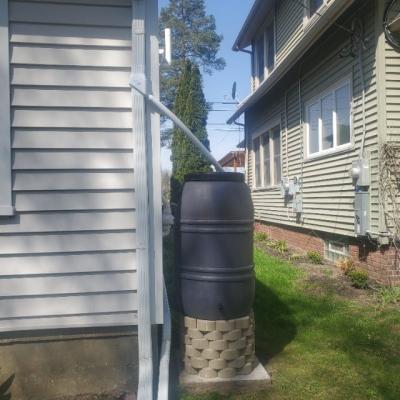 Grey rain barrel on paver blocks next to house with downspout diverter