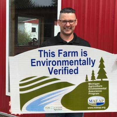 Farmer producer hold a "This Farm is Environmentally Verified" MAEAP sign